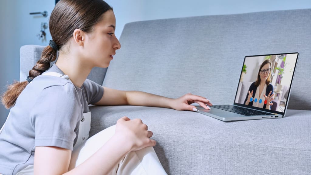 A person sits on the floor leaning against a couch, using a laptop for a video call. Curiously, they ask, "How much does BetterHelp pay therapists?" as another person visible on the screen listens attentively.